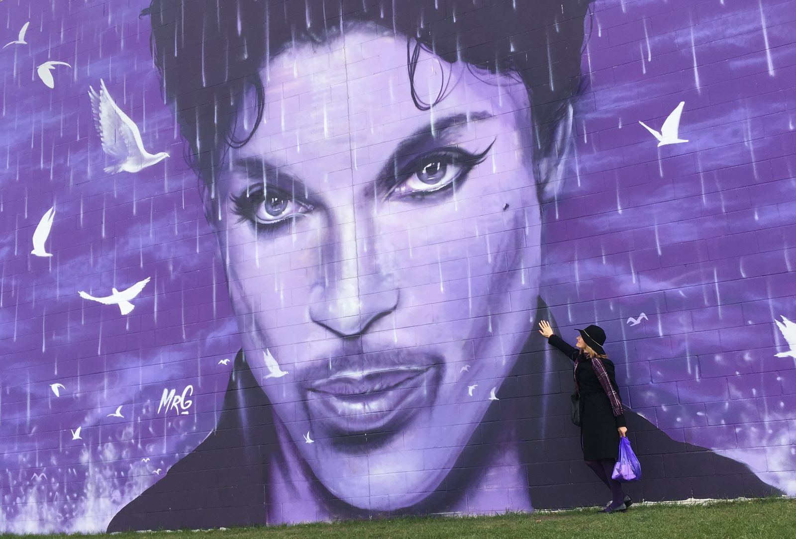 A woman in black touches a large purple mural of Prince's face